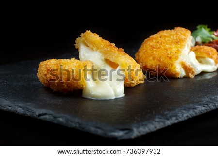 Breaded mozzarella cheese sticks laid out on a black slate. Close up.