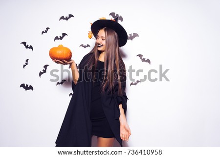 a young beautiful gothic girl in the shape of a witch in halloween, a big black hat decorated with yellow leaves, holding a pumpkin