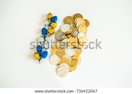 row of tiny dreidels and a pile of gold and silver Hanukkah coins isolated on white