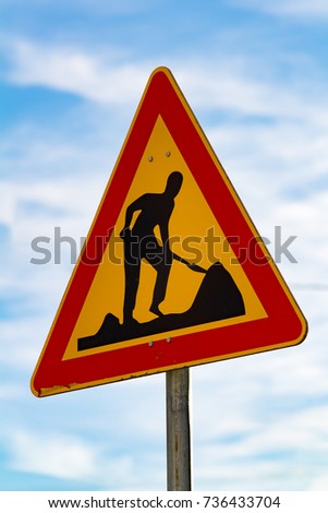 Closeup of a red and yellow construction yard warning sign on blue sky background