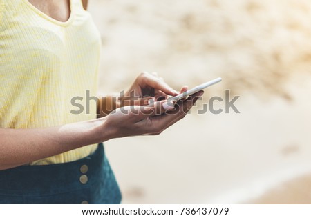 girl hold on smart phone gadget in sand coastline, mock up blank screen. Traveler using in female hand mobile on background beach seascape horizon. Tourist look on blue sun ocean, summer lifestyle 