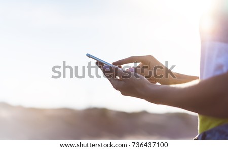 Hipster girl hold on smart phone gadget in sand coastline, mock up blank screen. Traveler using in female hand mobile on background beach seascape. Tourist look on blue sun ocean, summer lifestyle 