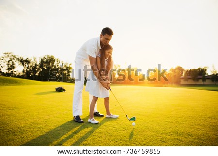 The man is standing behind the girl and concentrating her hands to hit the ball. The girl is holding a stick and is about to make a punch.