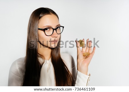 a beautiful long-haired girl with glasses is holding gold coins in her hands and looking into the camera. Bitcoins, crypto currency