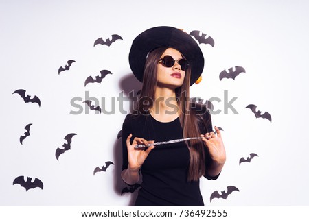 cute girl witch going to Halloween party and holds in his hands a magic witch's wand. Against the background of a bunch of bats
