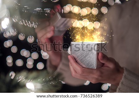 Female open Christmas gift box with ray of magic light on bokeh lights background.