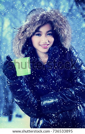 Portrait of young woman smiling at the camera while holding a cup of tea on the winter park
