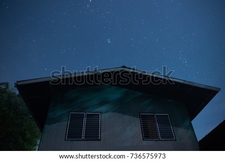 A night photo of a rural simple farmhouse and a starry sky above it.