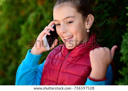 Happy smiling girl in a red waistcoat with a smartphone in her hand. The beautiful girl is emotionally happy with good news on the smartphone. Portrait smiles girl. copy space. 