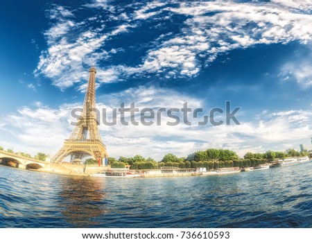 The Eiffel Tower in Paris, France, on a sunny day with Seine river and dramatic clouds.  Colourful travel background. Popular travel destination