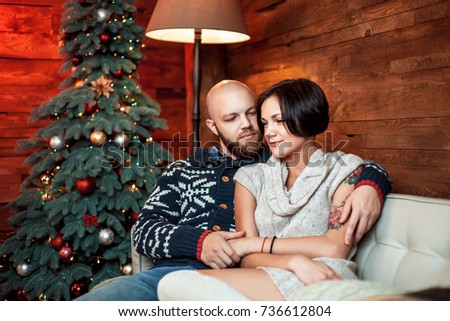 Beautiful couple sitting on the couch embrace in a decorated festive interior with a Christmas tree. The concept of a family celebration, new year's eve