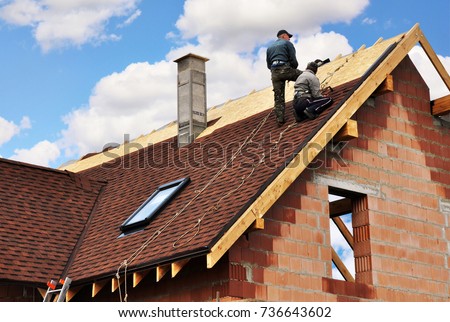 Roofers laying and installing asphalt shingles. Roof repair with two roofers. Roofing construction with roof tiles, asphalt shingles. Royalty-Free Stock Photo #736643602