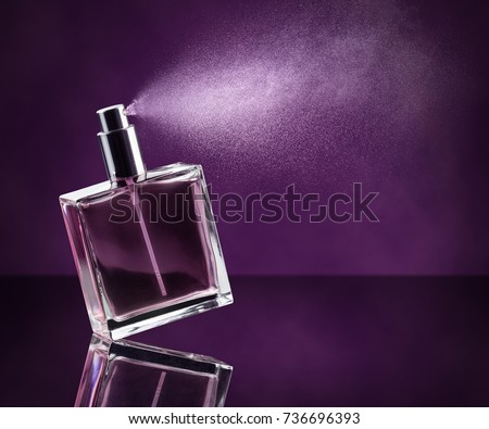 perfume bottle spraying on dark purple background Royalty-Free Stock Photo #736696393