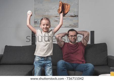 Daughter happy for favorite baseball team, father sitting unhappy