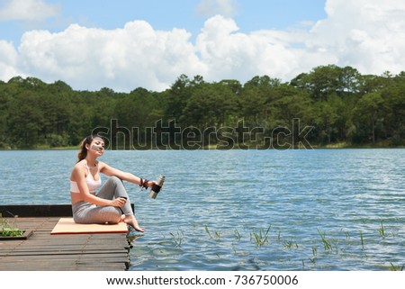 Pretty woman in sport clothes enjoying morning by the lake and drinking hot tea