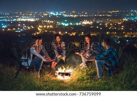 The young people warming near a bonfire on a city lights background. night time