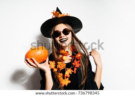 Beautiful halloween girl with long hair and good make-up and pale skin. A halloween woman in a black retro halloween dress and hat  holds a small pumpkin in his hands