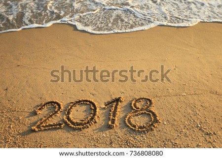 New Year 2018 is coming concept - inscription 2017 and 2018 on a beach sand, the wave is starting to cover the digits 2017 Royalty-Free Stock Photo #736808080