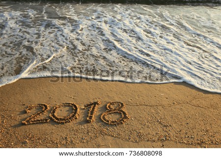 New Year 2018 is coming concept - inscription 2017 and 2018 on a beach sand, the wave is starting to cover the digits 2017 Royalty-Free Stock Photo #736808098