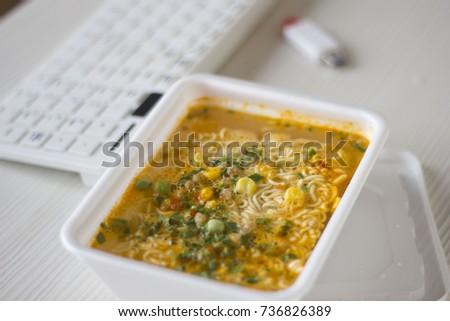 Chinese noodles on the desktop next to the keyboard. Eating instant noodles on work desk. food is on the desktop