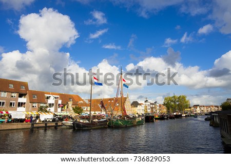 Netherlands Leiden Galgewater 3 October 2017, a bright blue sunny day and white clouds and old big boats with dutch flags in the harbor in the city canal with traditional dutch houses at the side