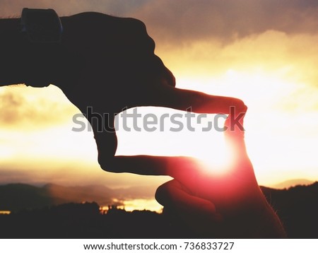 Close up of hands with watch making frame gesture. Dark misty valley bellow in landscape. Sunny autumn daybreak in mountains.