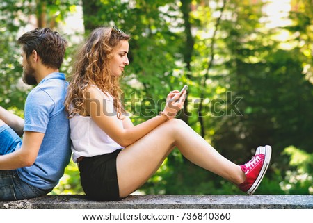 Young couple with smartphones in town sitting on concrete wall.