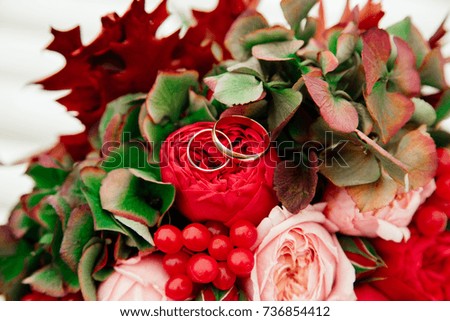 Wedding rings on the bouquet with red and pink roses and cranberries