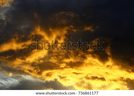Yellow and orange bright light on a group of cloud at sunset creates a strong contrast with the dark sky