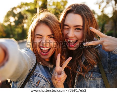 Two happy young brunette woman having fun while taking selfie on mobile phone, outdoor