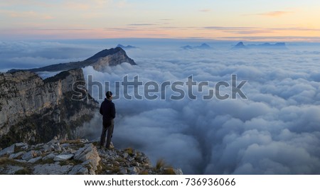 A hiker looking over a sea of clouds in the mountains at dawn.  Royalty-Free Stock Photo #736936066