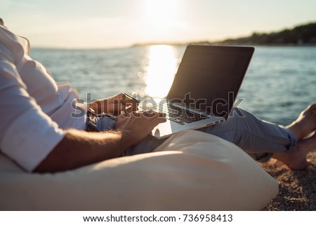 Senior man working on his laptop on the beach during sunset. Close up