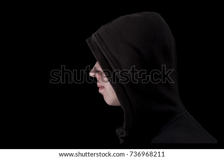 Young teenage bully boy in black hoodie isolated on black background for copy writing