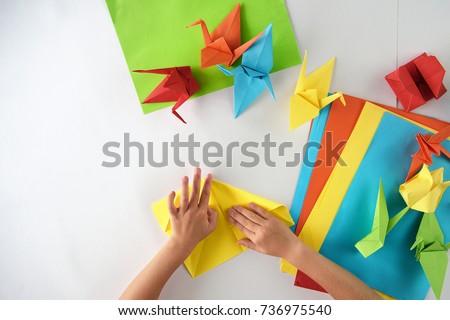 Children's hands do origami from colored paper on white background. lesson of origami Royalty-Free Stock Photo #736975540
