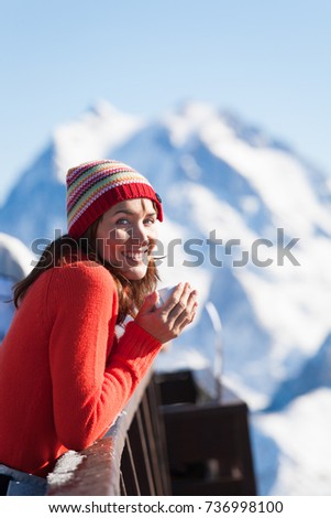 smiling woman drinking a hot drink on a terrace in snowy mountains