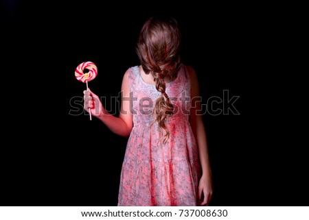 Portrait of  girl without a face in dress ready for halloween night with a candy bar in her hand on a black background. 