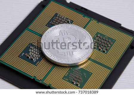 silver bitcoin. a computer processor. a black disk on a light wooden background