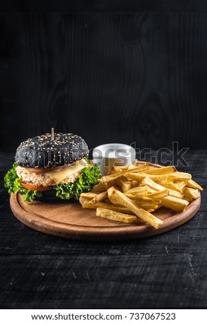 Tasty black bun burger with french fries and sauce on the black wooden surface.