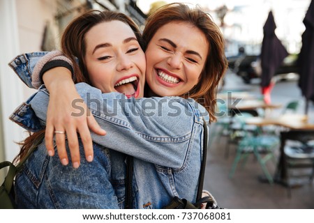 Close-up photo of laughing woman friends hugging each other on city street Royalty-Free Stock Photo #737068081