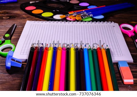 Set of different school stationeries. Notepad, scissors, pensils, paints, paintbrushes on rustic wooden desk. Back to school