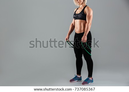 Cropped image of a fit muscular adult sportswoman holding stretching band isolated over gray background