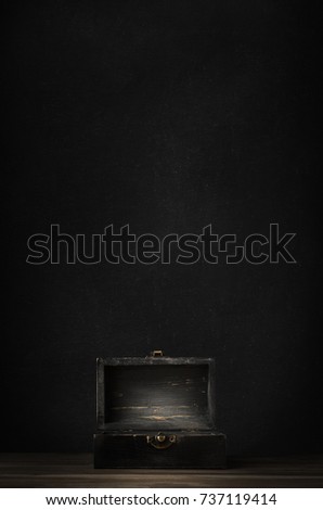 A dark wooden treasure chest with lid open and lit on planked surface with black chalkboard background.