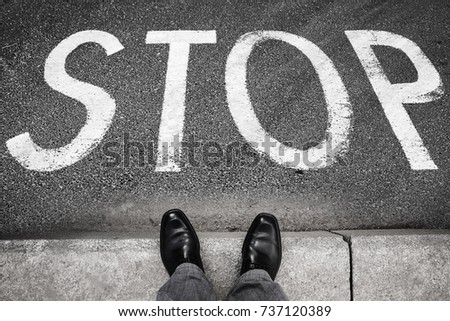 Feet of a man in black shining shoes standing opposite stop road marking