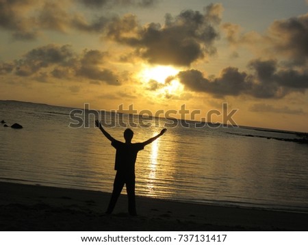 Triumphant silhouette in front of a gorgeous sunrise over La Playa Almendra (Almond Beach) in the Galapagos.                               