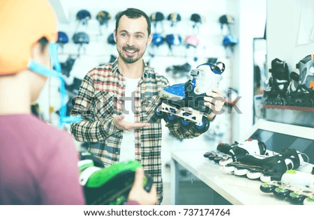 Positive male seller demonstrating roller-skates to boy customer in sports store
