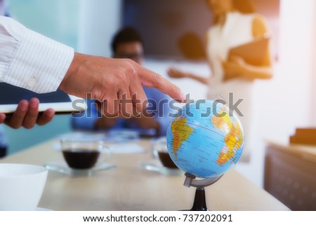 Portrait of businessman pointing his finger at the globe to determine a business investment point with a backdoor is a meeting.