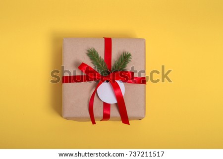 Gift kraft square box with a red ribbon on a yellow background with the wishes of Happy New Year. flatlay