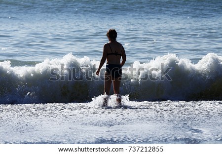 In bright sunlight the silhouette of a woman faces the bubbling boiling surf of a breaking wave. Royalty-Free Stock Photo #737212855