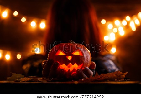 Photo of witch with long hair holding halloween pumpkin in background with burning garlands