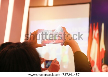 Blur of woman hands take photo or recording speaker with smart phone, camcorder mobile operator working for record speaker on stage in conference and convention hall.
